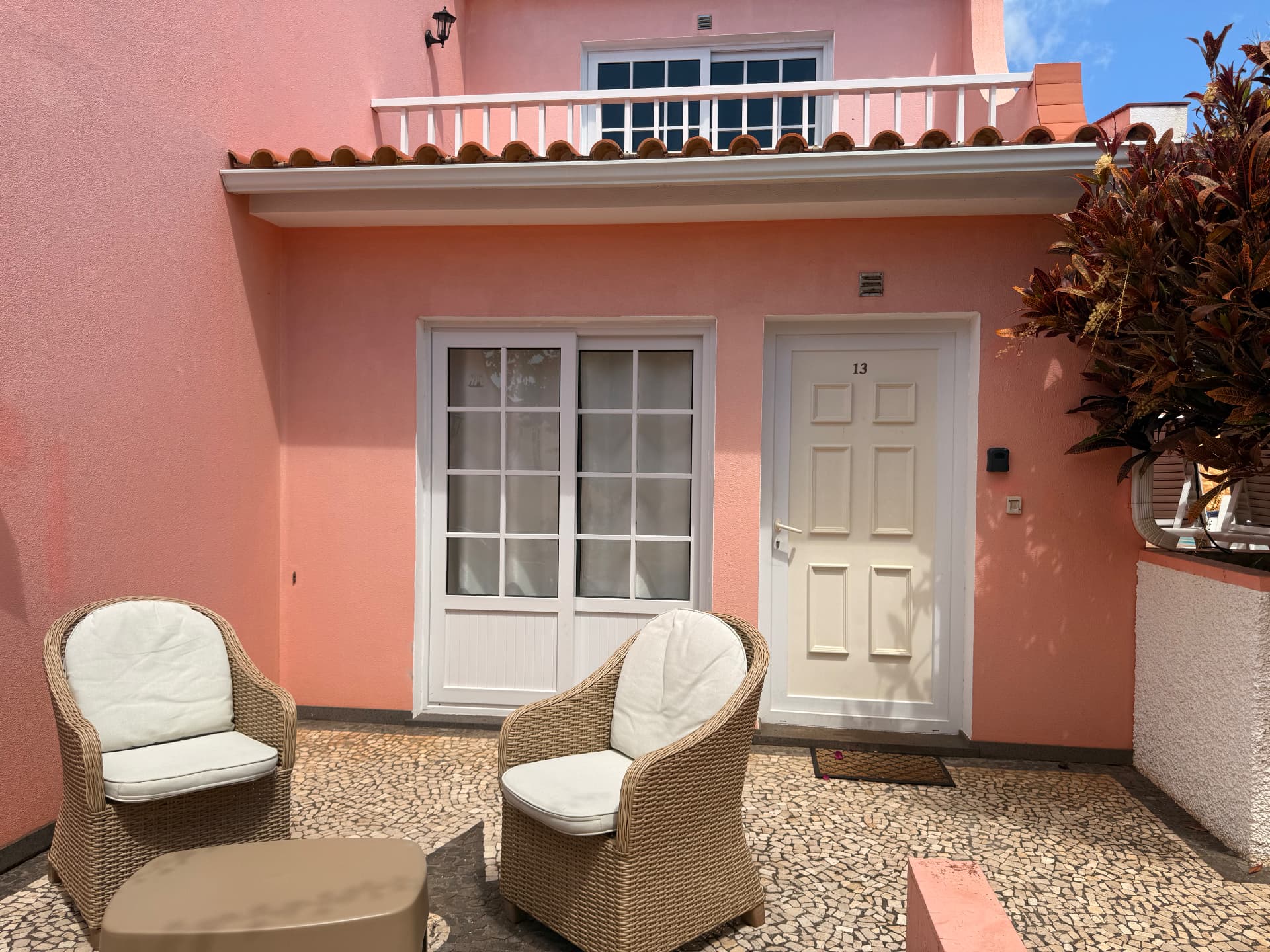 Private cobblestone patio of a pink-walled villa with wicker armchairs and white-trimmed glass doors