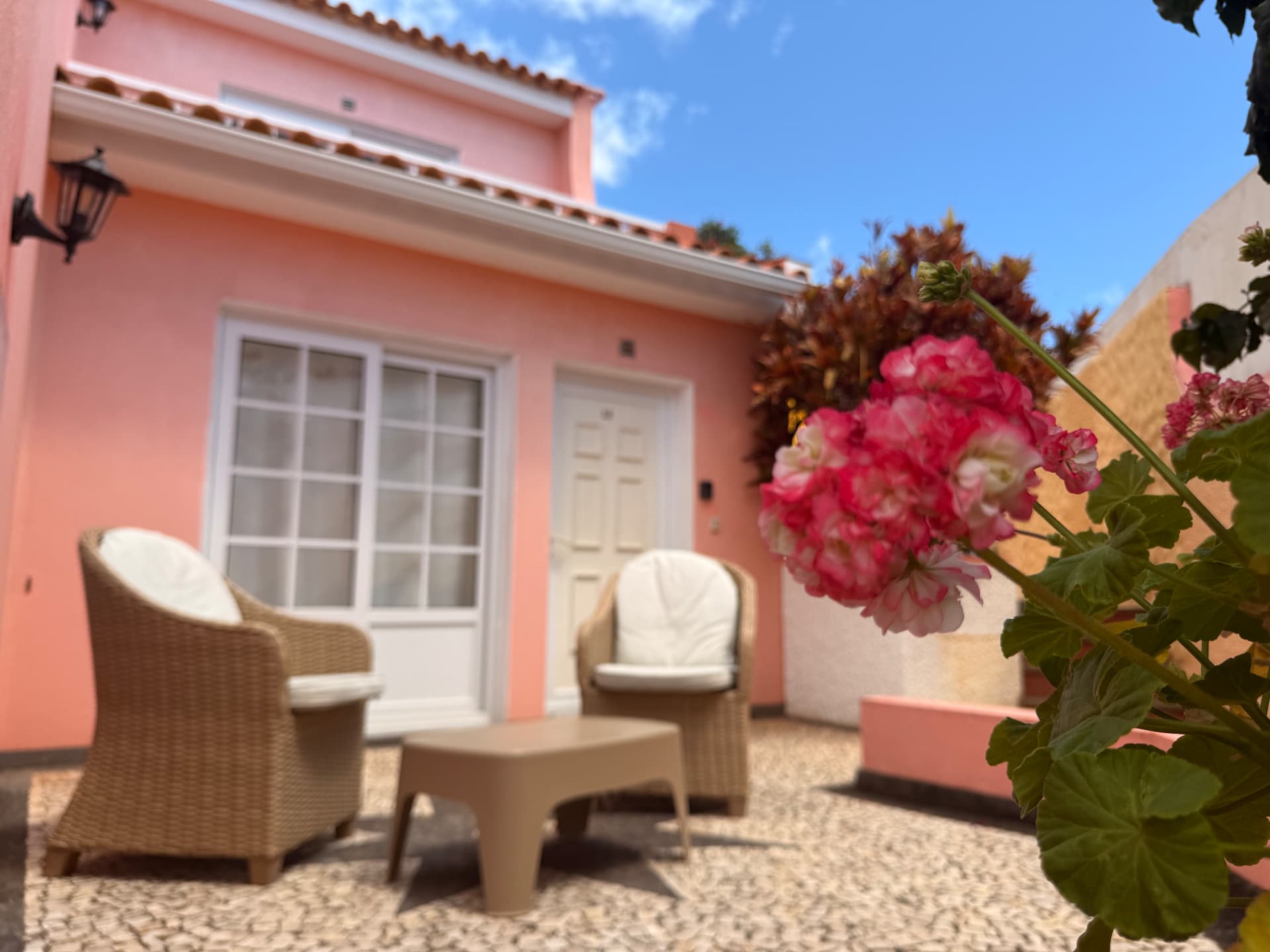 Villa terrace with tan wicker armchairs, white cushions and a pink wall with glass door