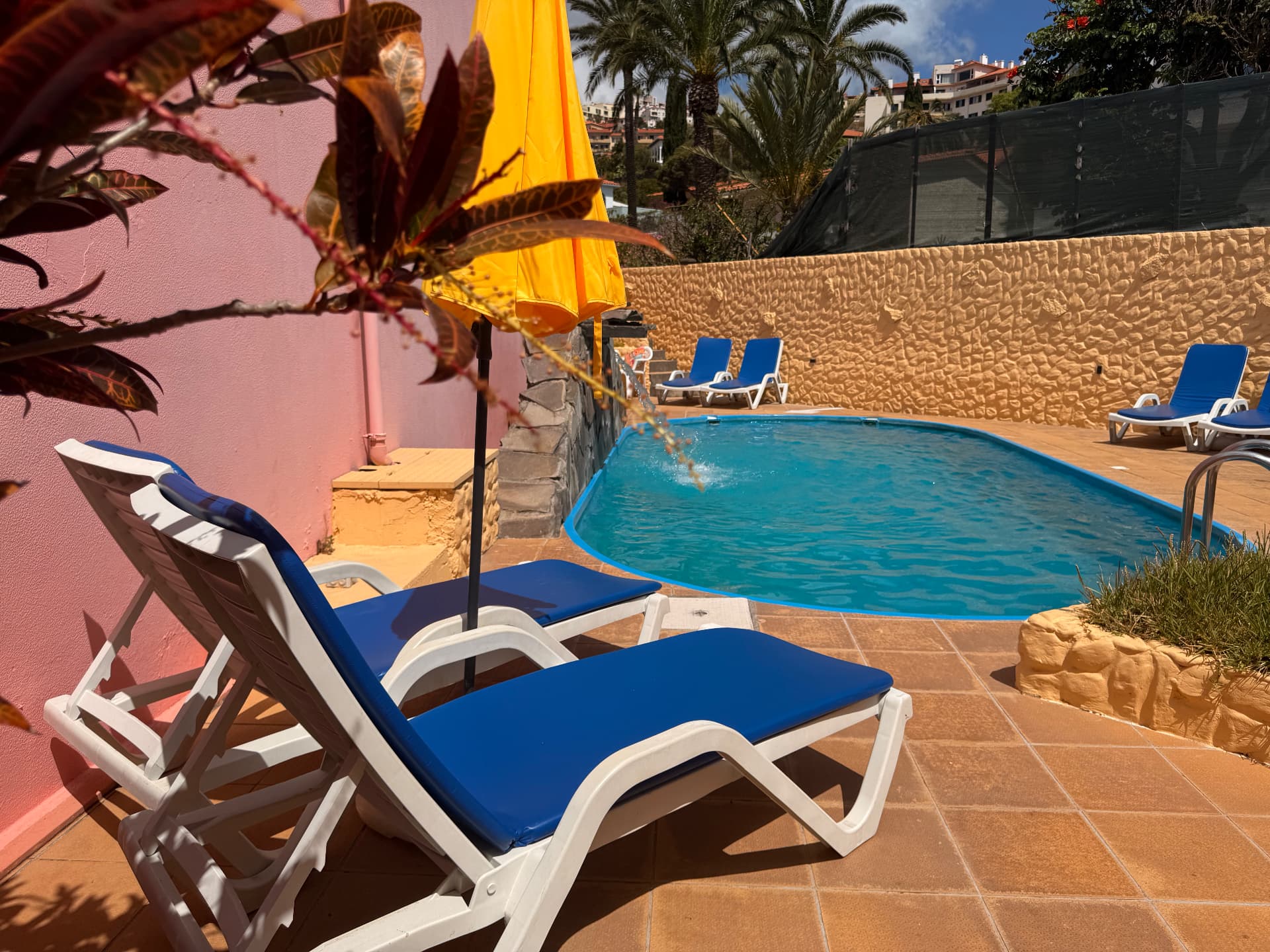 Pool terrace with blue-cushioned lounge chairs, yellow sun umbrella and terracotta tiles