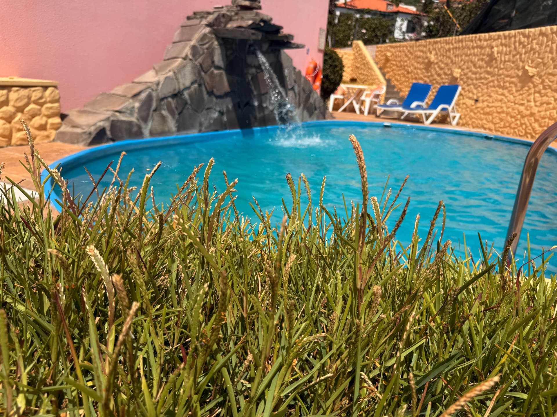 Swimming pool with stone waterfall feature against pink and mustard walls at Falesia Gardens