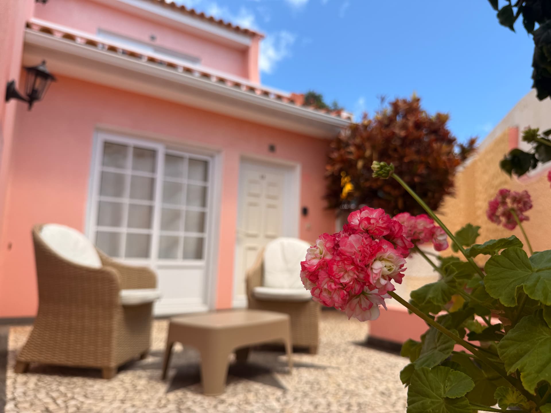 Pink and white geranium blossoms framing the villa patio and wicker chairs beyond